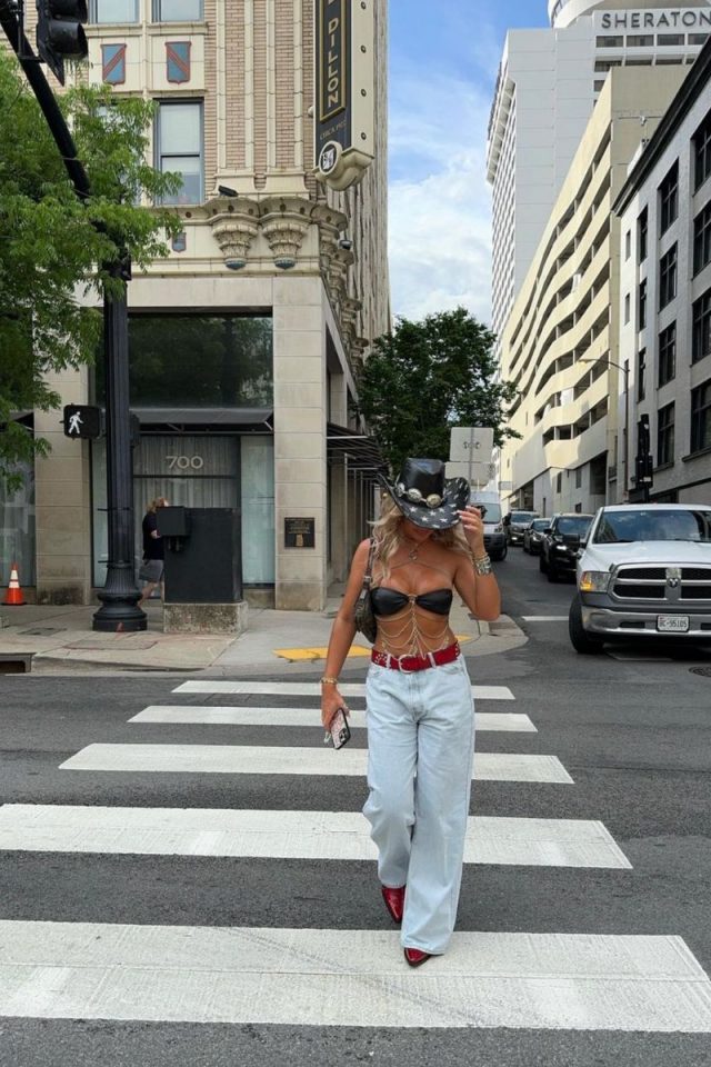 Urban Cowgirl This bold outfit is perfect for making a statement in Nashville. It features a black bandeau top accented with gold chain details, paired with high-waisted, light-wash jeans. The look is completed with a black cowboy hat adorned with silver embellishments, a red belt, and striking red cowboy boots. This outfit is ideal for a night out on Broadway, combining urban flair with classic western elements. Discover stylish and practical Nashville outfit ideas perfect for every activity, from brunch and exploring to concerts and nightlife. Get inspired with our fashion tips for your next trip to Music City! Nashville Outfits, Nashville Outfit, Nashvile Outfit, Nashville Outfit Summer, Nashville Outfits Summer, Nashvile Outfit Summer, Nashville Bachelorette Party, Spring Outfit, Concert Outfit, Country Concert Outfit, Date Night Outfit, Music Festival Outfit, Country Concert Outfit Ideas